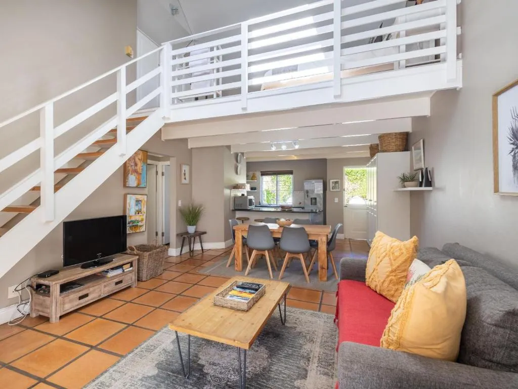 Double-volume living room with a white staircase to the mezzanine bedroom and a dining table