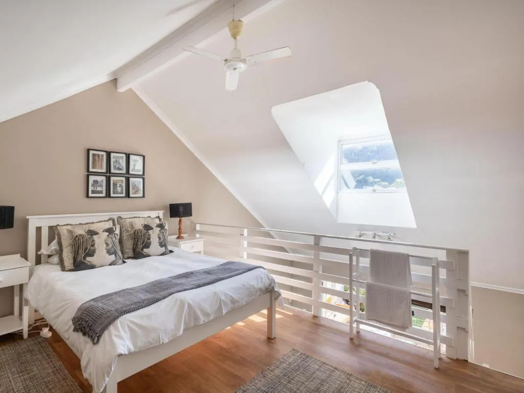 Loft bedroom under a skylight with a ceiling fan and a mezzanine railing