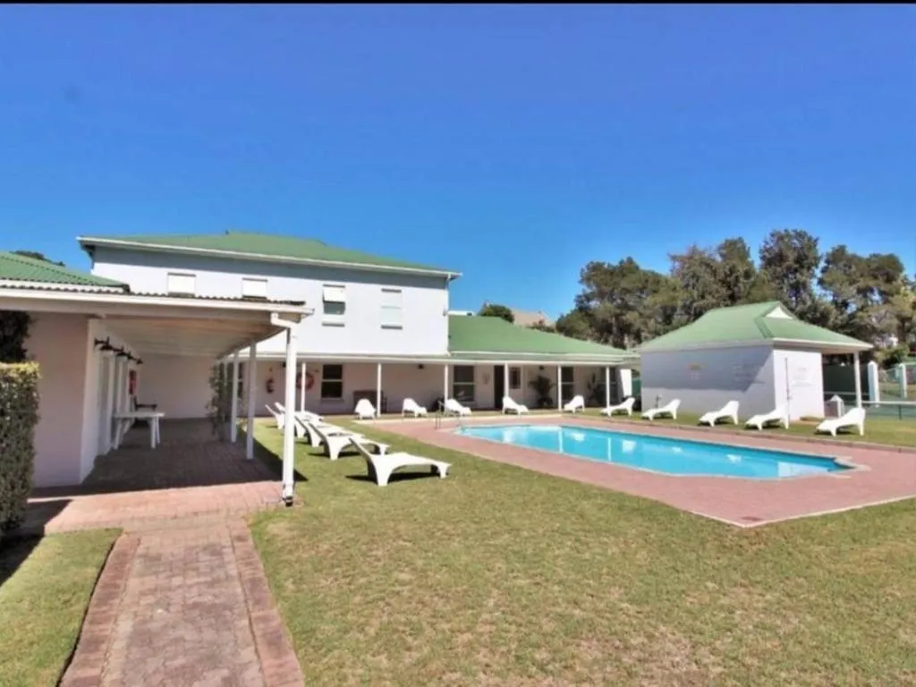 Shared estate pool with sun loungers, a clubhouse, and tennis courts beyond