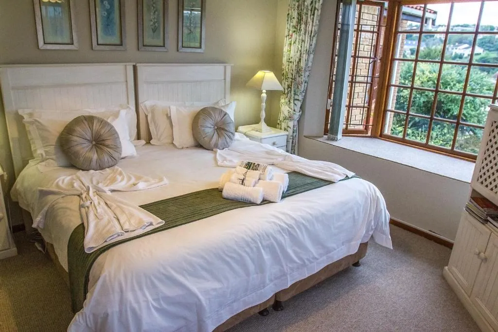 Twin beds dressed with rolled towels, floral prints, and a bay window overlooking the garden