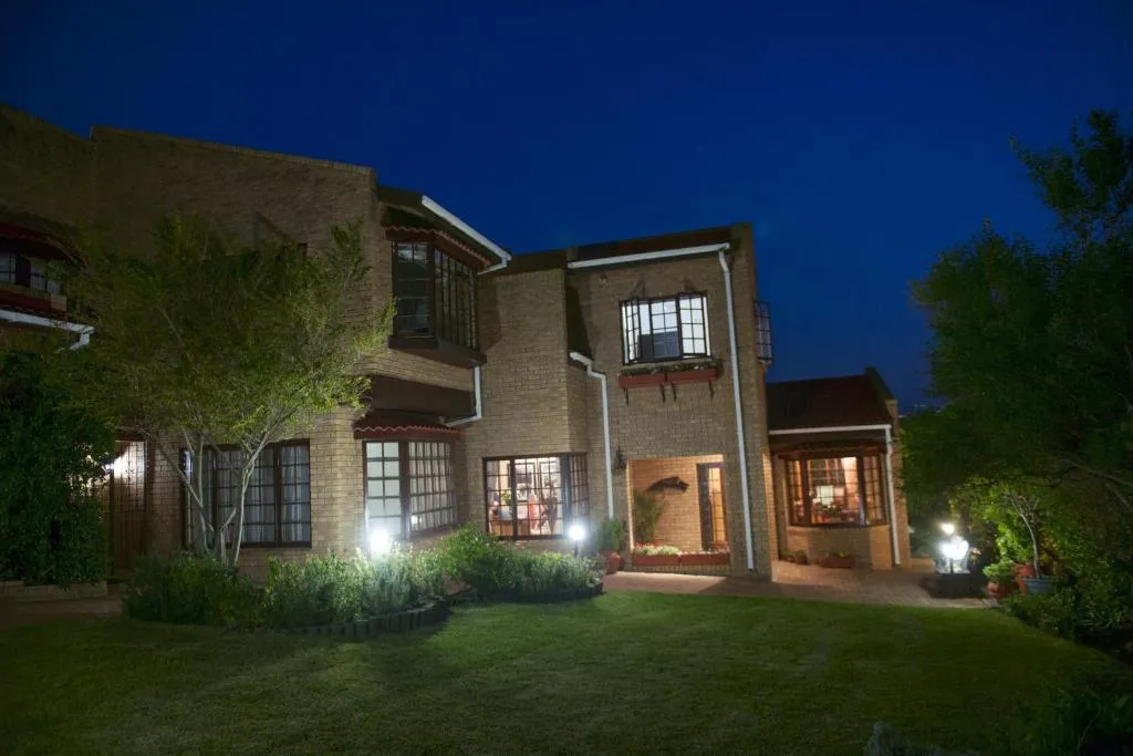 Cape Dutch-style double-storey guesthouse lit up at dusk with a lawned garden in front