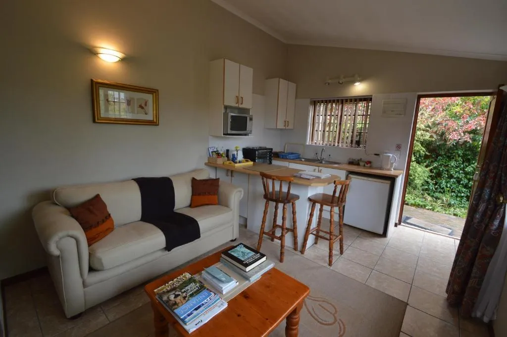 Self-catering lounge with a cream sofa and a small kitchenette opening onto the garden