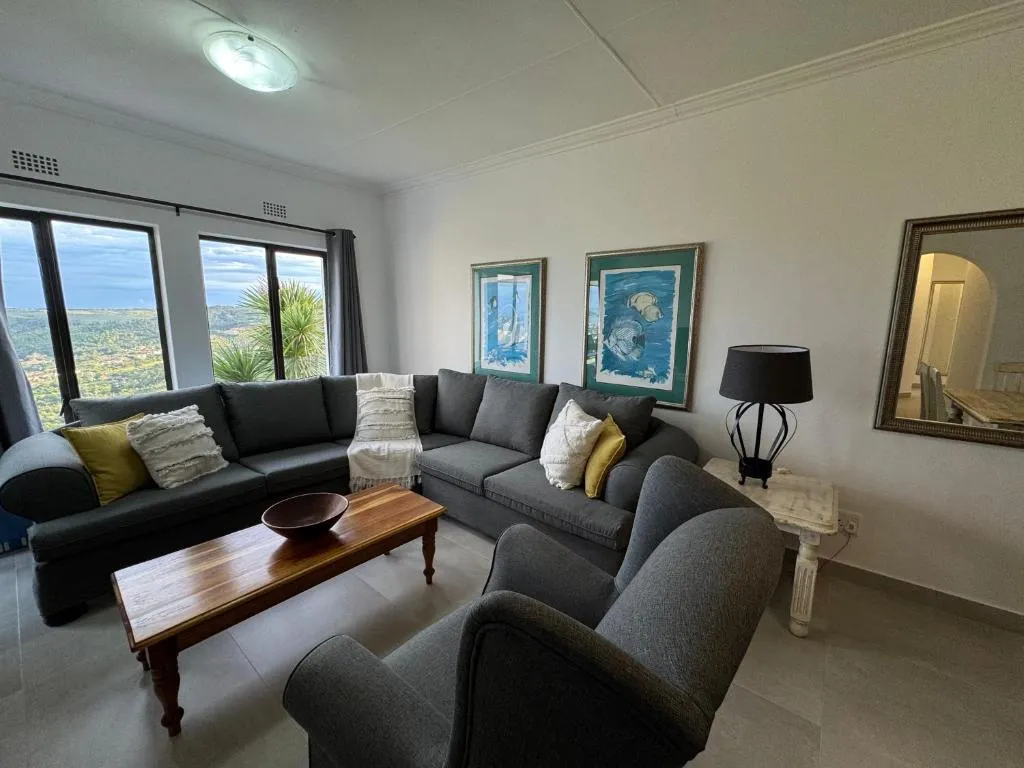 Living room with a grey L-shaped sectional, framed fish prints and windows onto the hillside view