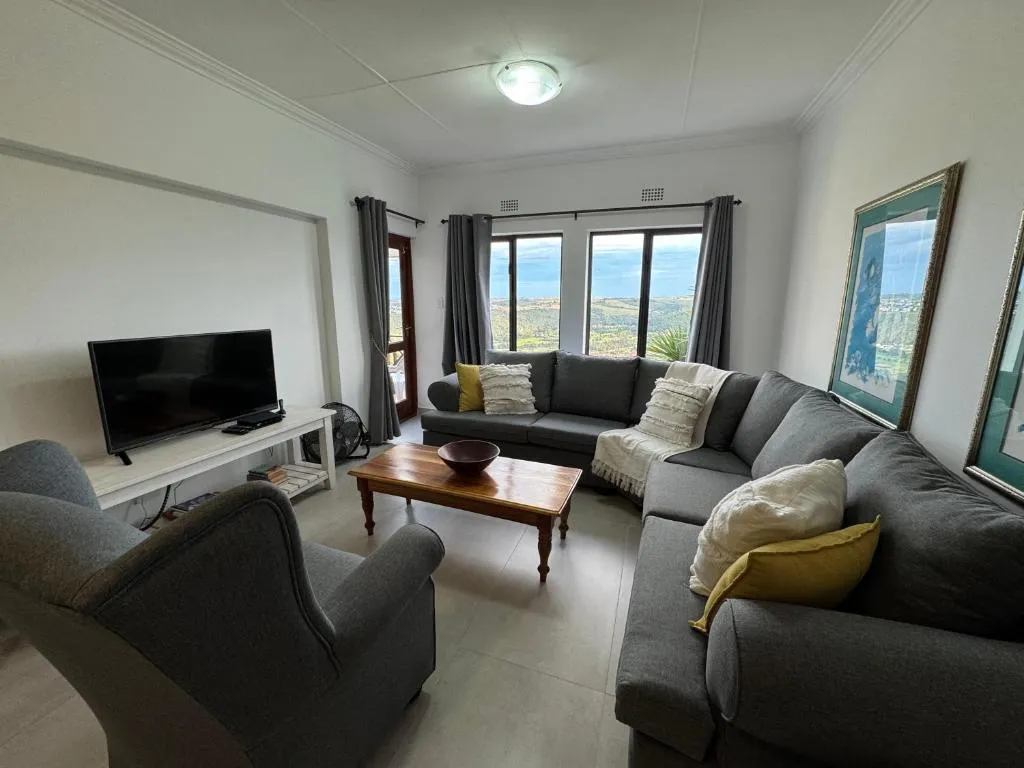 Second view of the living room showing the TV unit, armchair and windows with a hint of distant water
