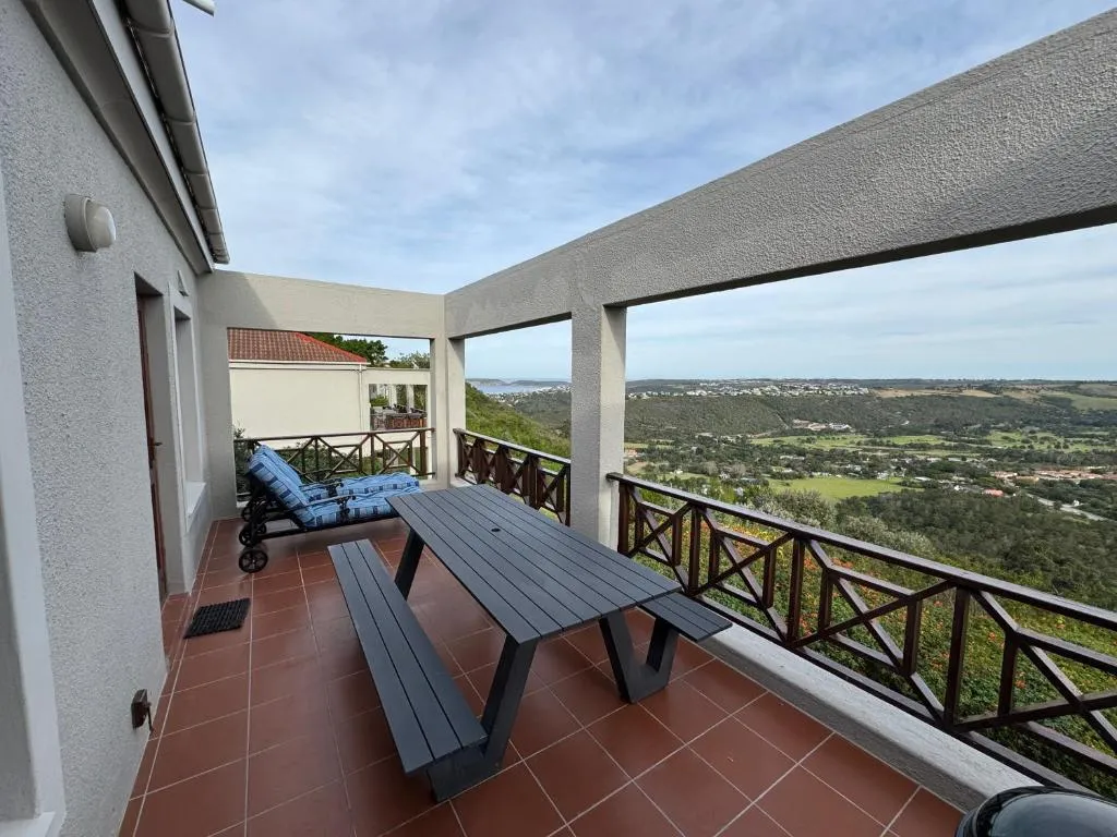 Covered terrace with a picnic-style table and lounger, looking out over the hillside to the lagoon and coast
