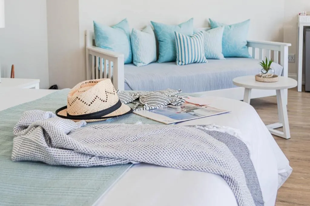 Bed styled with a straw hat and striped beach towels beside a pale blue scatter-cushion bench