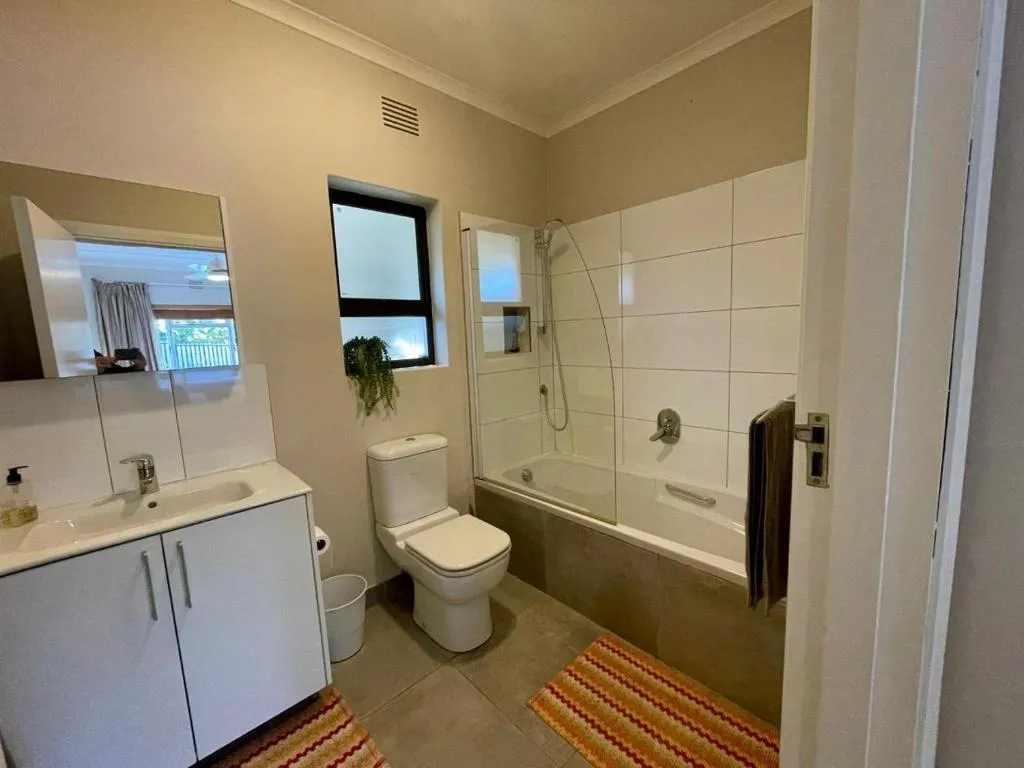Bathroom with a bath-shower combo, tiled surround, and a frosted window with a hanging plant