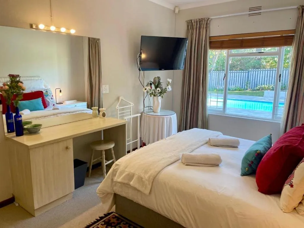 Bedroom with red and teal cushions, a wall-mounted TV, and a window overlooking the pool