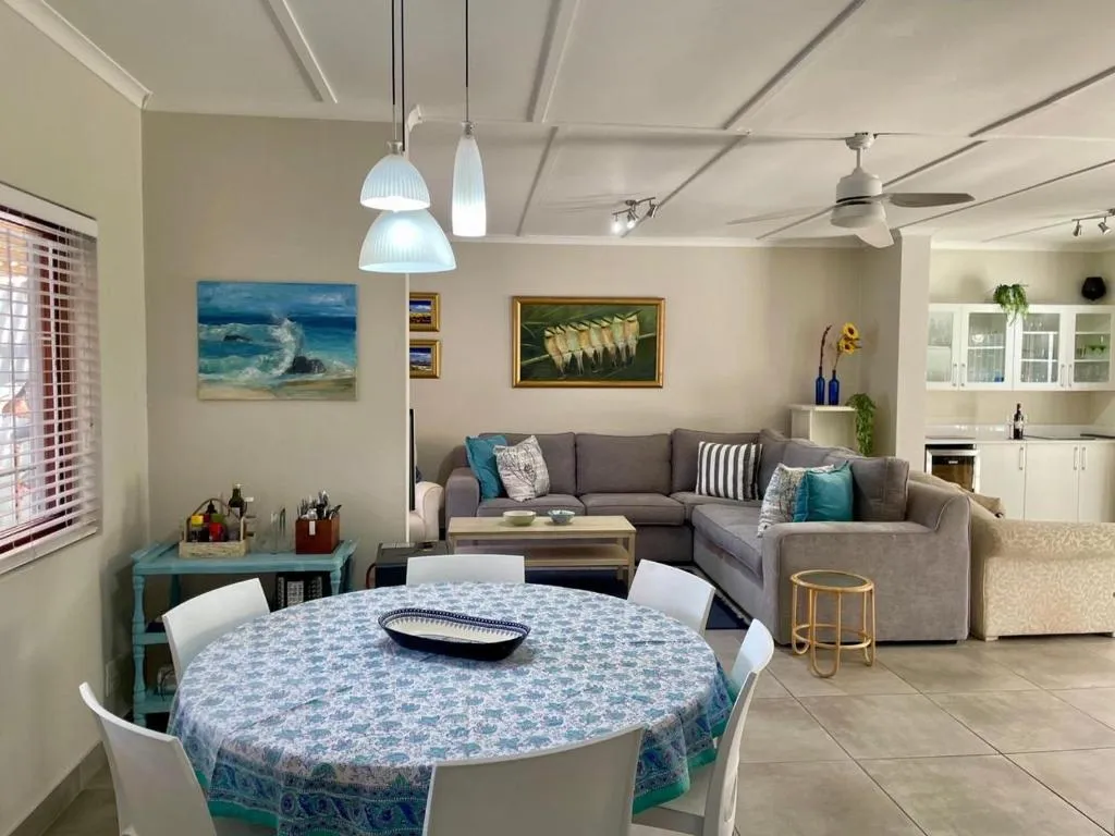 Open-plan living and dining area with a grey corner sofa, round dining table, and open kitchen