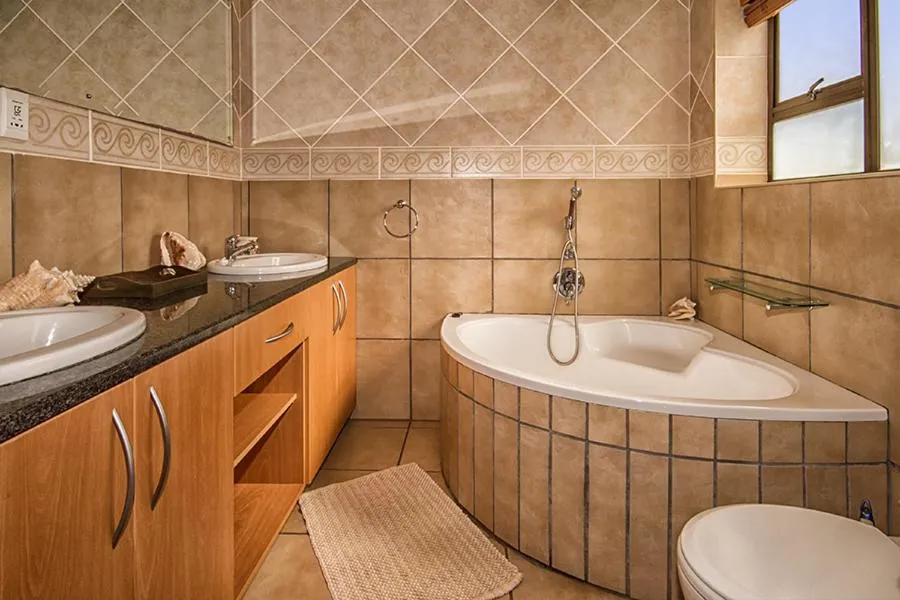 Bathroom with a corner spa bath, twin vanity sinks and a decorative mirror