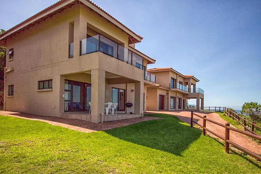 Double-storey home exterior with a covered patio, kettle braai and manicured lawn