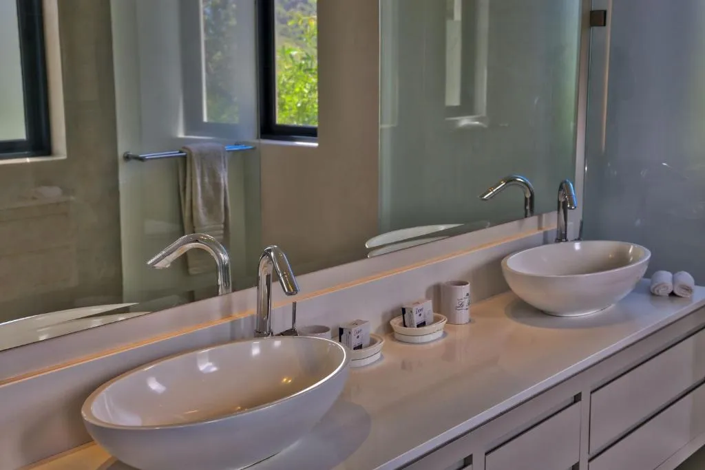 Bathroom with twin vessel basins, a wide mirror, and a window onto greenery