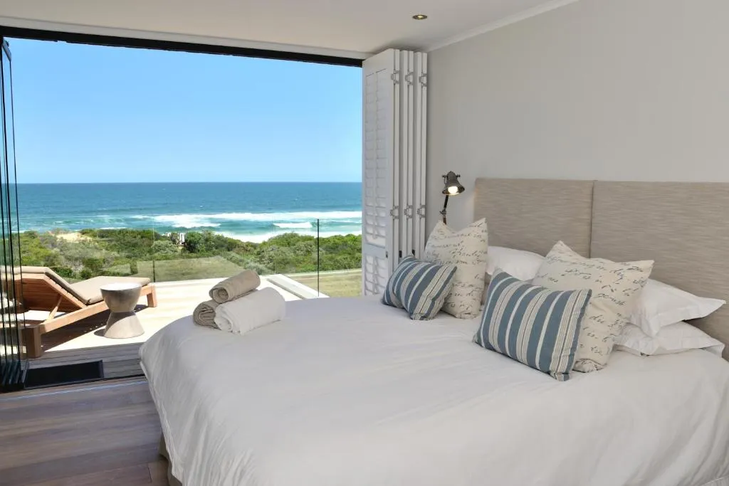 Bedroom with glazed doors folded open to a balcony daybed and uninterrupted sea view