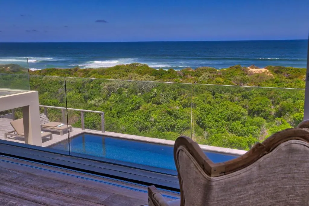 Poolside armchair facing an infinity-edge pool with breaking waves beyond the dunes