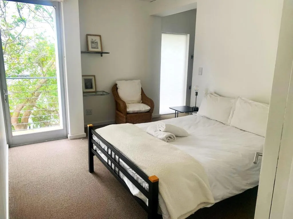 Bedroom with sliding doors onto a tree-shaded balcony, a wicker chair and black metal bed frame