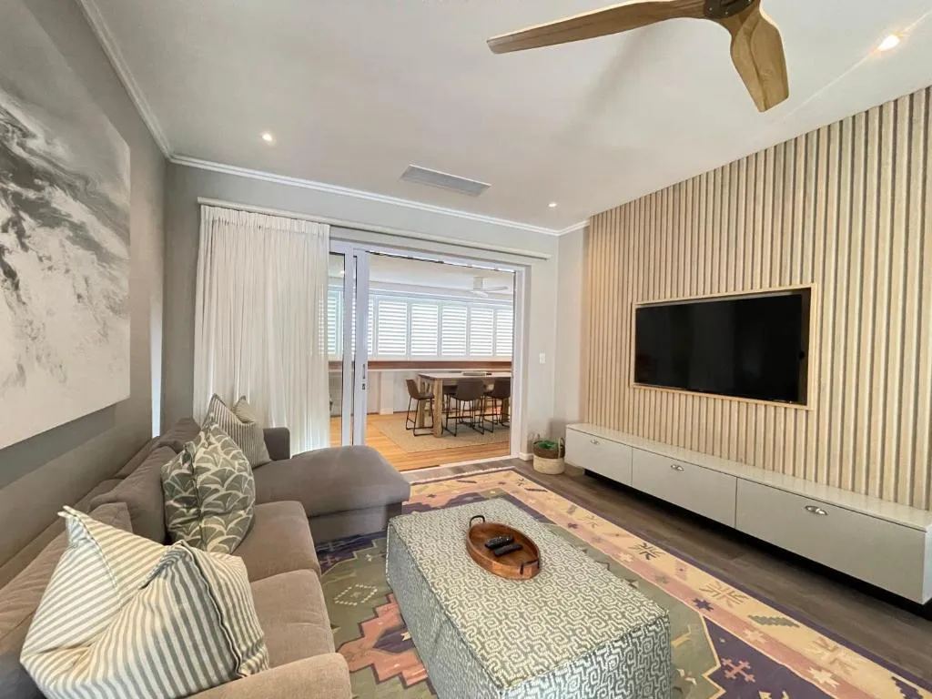 Open-plan living room with grey sofa, striped cushions and TV mounted on a slatted timber wall