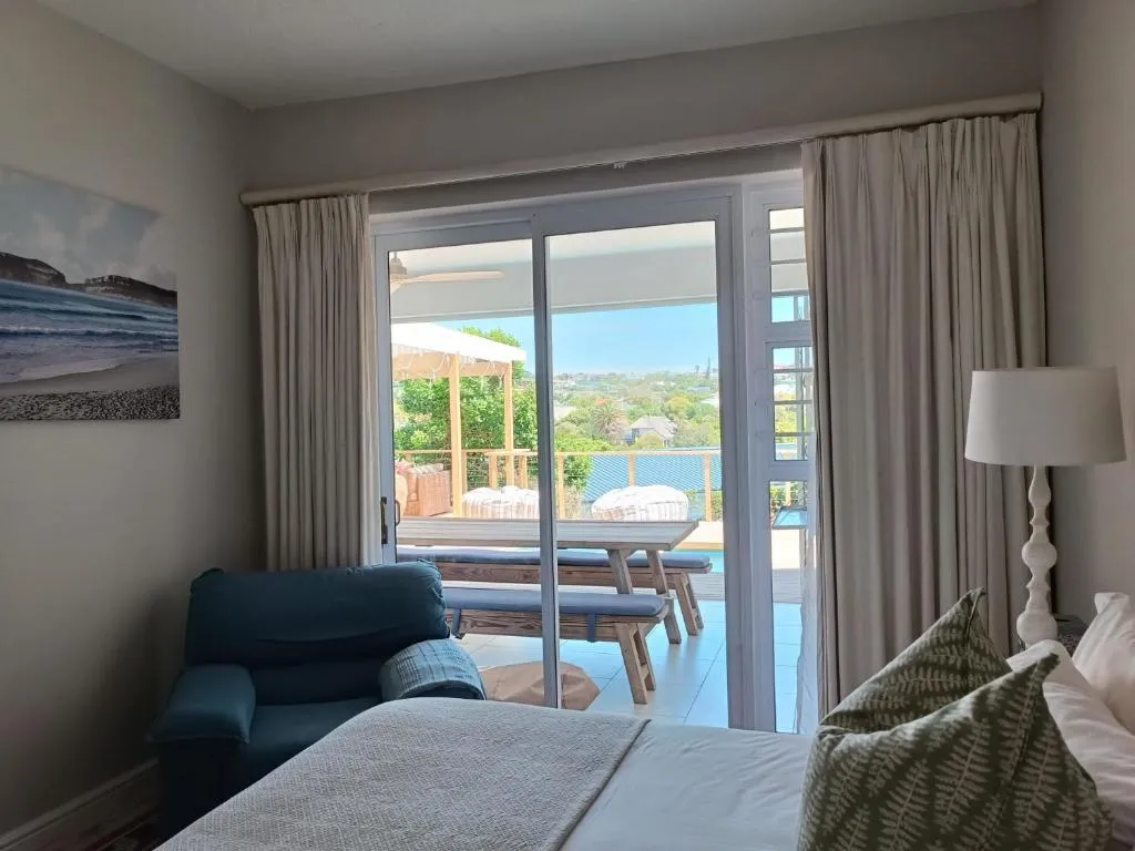 Bedroom with a blue armchair and sliding doors opening onto the pool deck and dining terrace