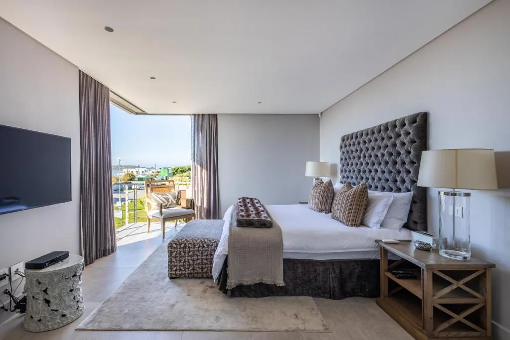 Main bedroom with a tufted headboard and sliding doors opening onto a balcony overlooking the coast