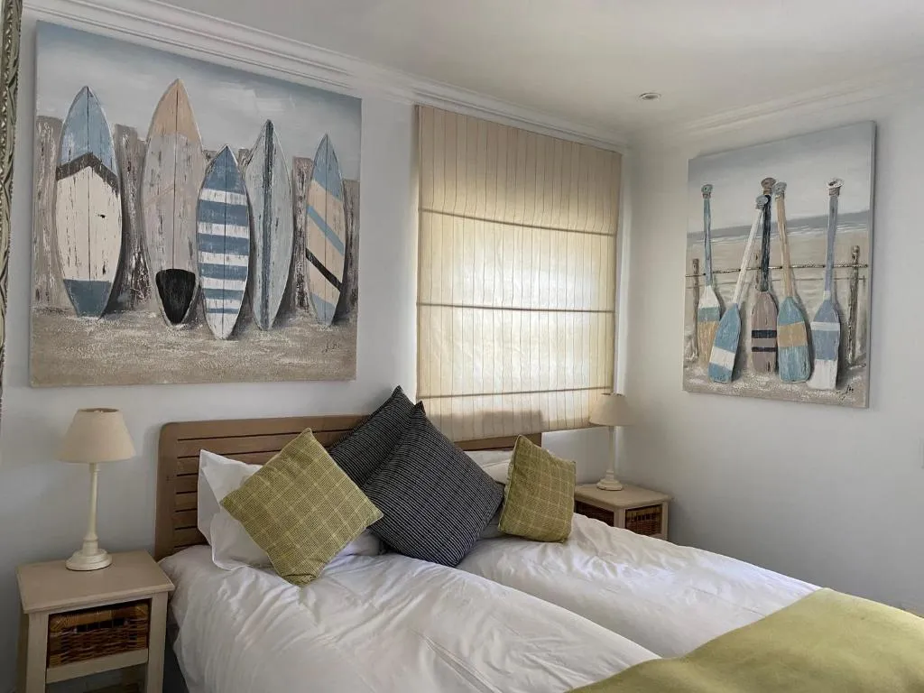 Twin bedroom with surfboard and paddle wall art above pale timber headboards