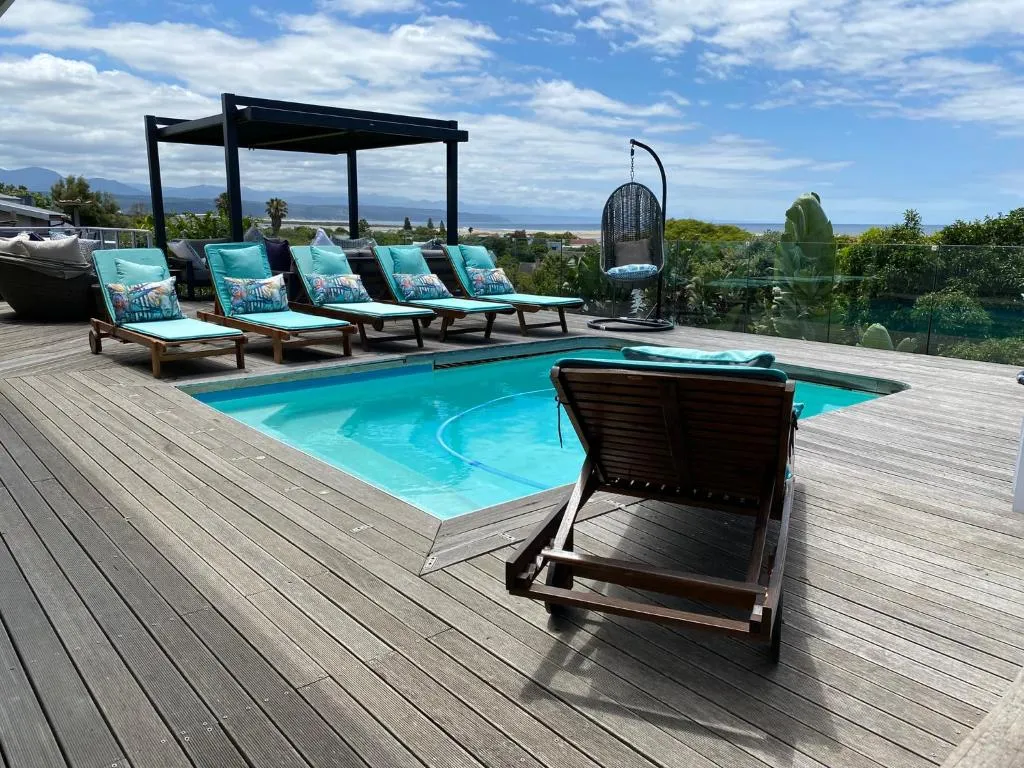 Wooden pool deck with loungers and a hanging chair overlooking the beach and ocean
