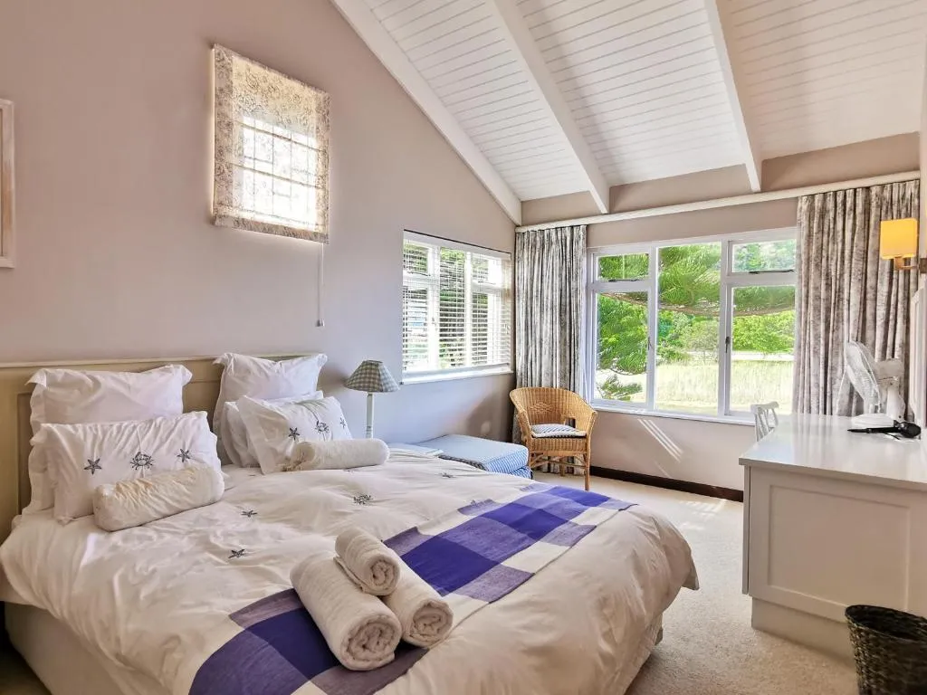 King bedroom with tartan throw and rolled towels, sash windows looking onto a garden of pines