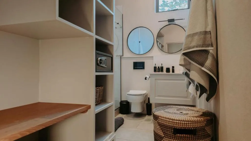 Walk-in bathroom with a wall safe, wicker hamper, and round mirrors over a floating vanity