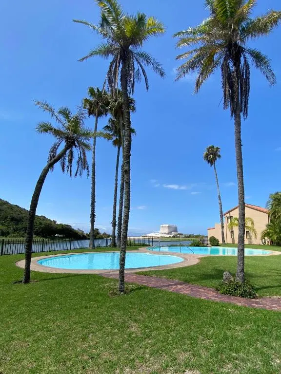 Lagoon-shaped communal pool framed by tall palms, with the Keurbooms estuary and Beacon Island beyond