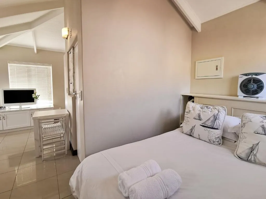 Bedroom with nautical-print cushions, white linen and a partial view into the lounge