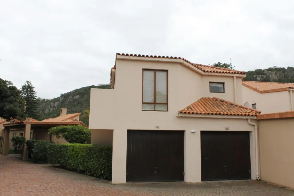 Terracotta-roofed townhouse block with double dark-wood garage doors and a hillside backdrop