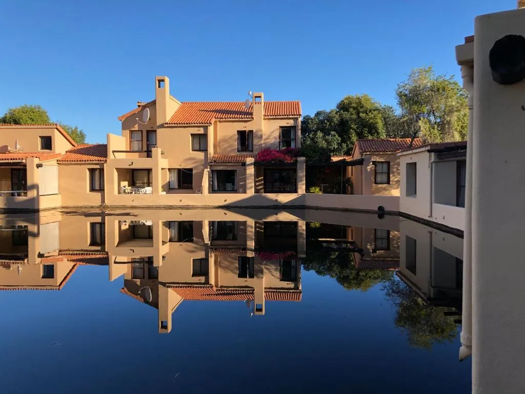 Exterior view of the estate's terracotta-roofed units reflected in the still lagoon