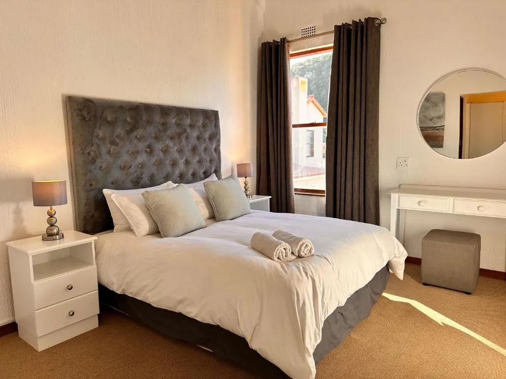 Bedroom with a tufted grey headboard, round mirror and dressing table below a window