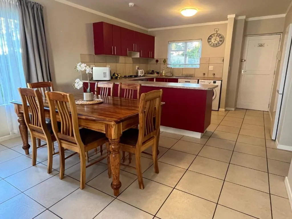 Dining table beside a red-cabinet kitchen with a gas hob, microwave and wall clock