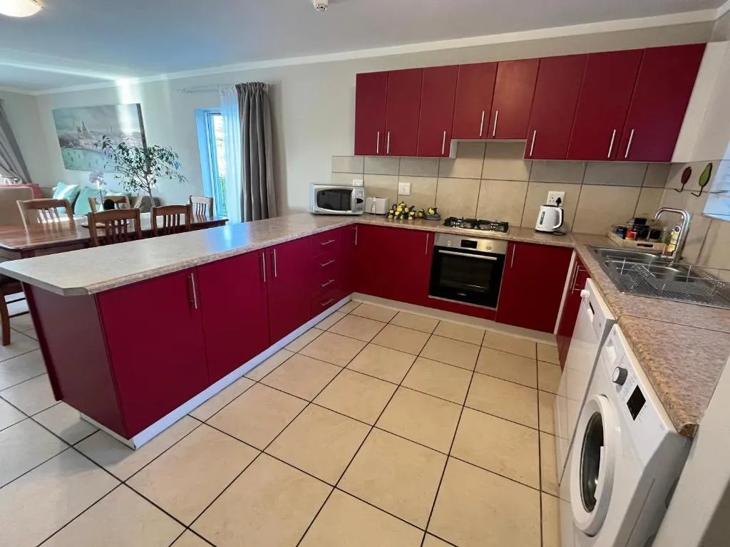 L-shaped red kitchen with a gas stove, built-in oven, dishwasher and front-loader washing machine