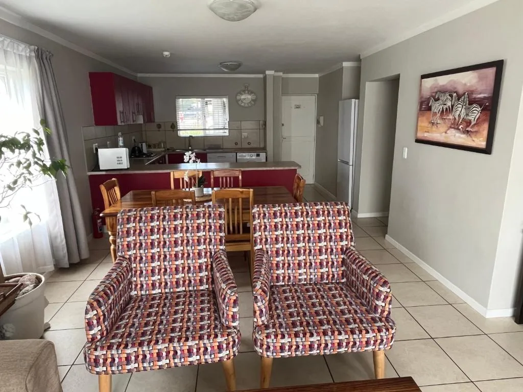Dining and lounge area with woven patterned armchairs and an open kitchen pass-through behind