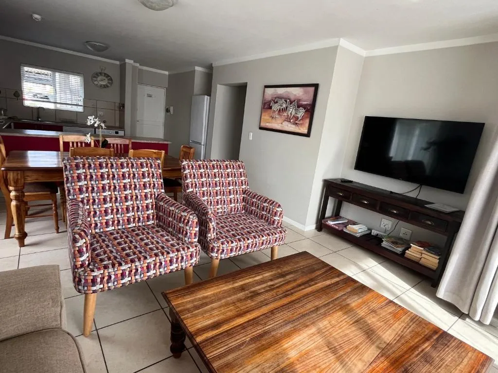 Lounge corner with woven patterned armchairs, a wall-mounted TV and a console table of books