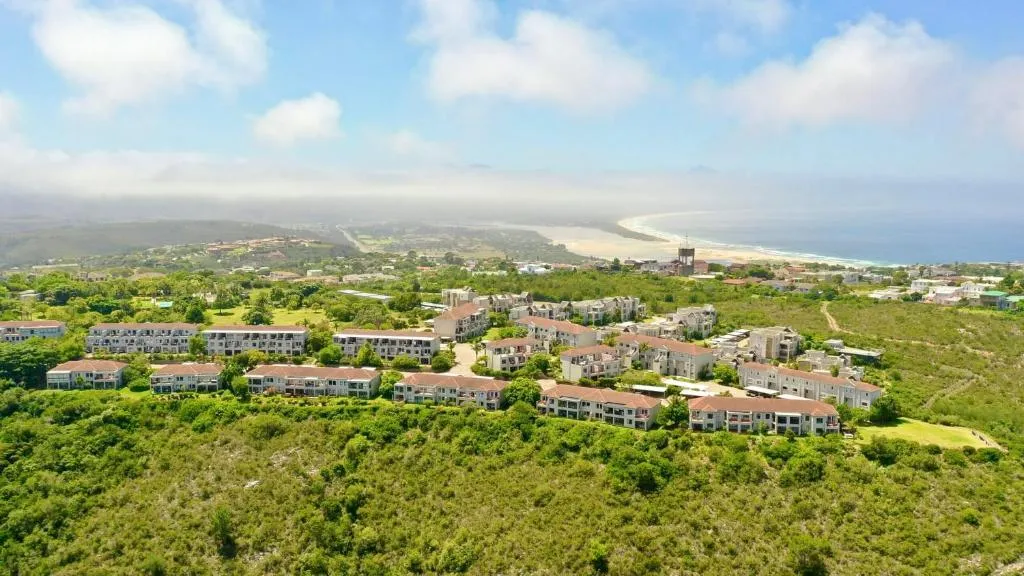 Aerial view of the complex's rooftops with the beach and coastline visible through haze