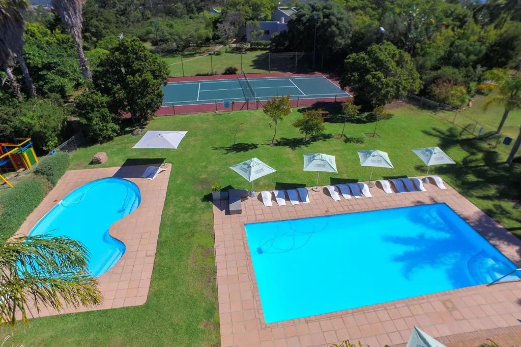 Aerial view over the estate's tennis court, pool and sun-lounger terrace framed by palms
