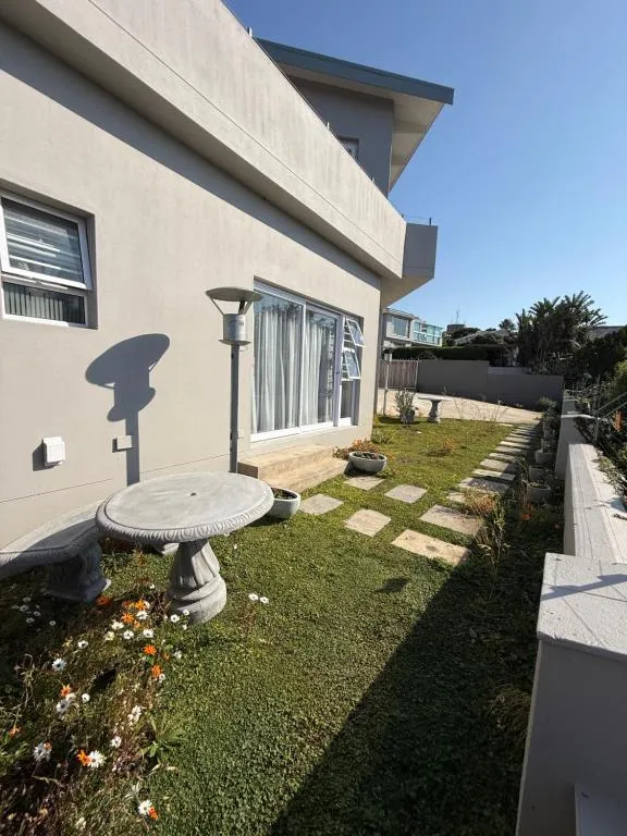 Paved garden path past a stone birdbath and bench, with the guesthouse balcony above