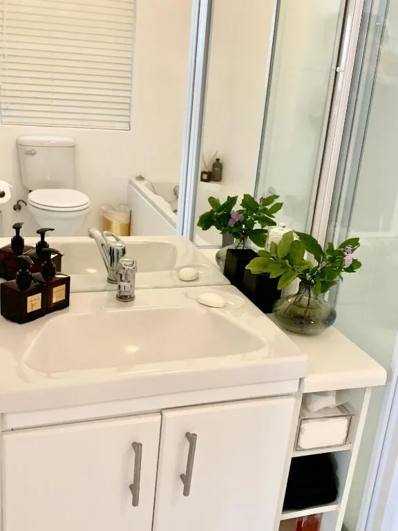 Compact bathroom vanity with twin taps, amenities and a tub visible in the mirror behind
