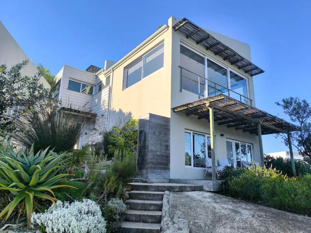 Multi-level house exterior with a slatted timber pergola deck and steps through fynbos planting