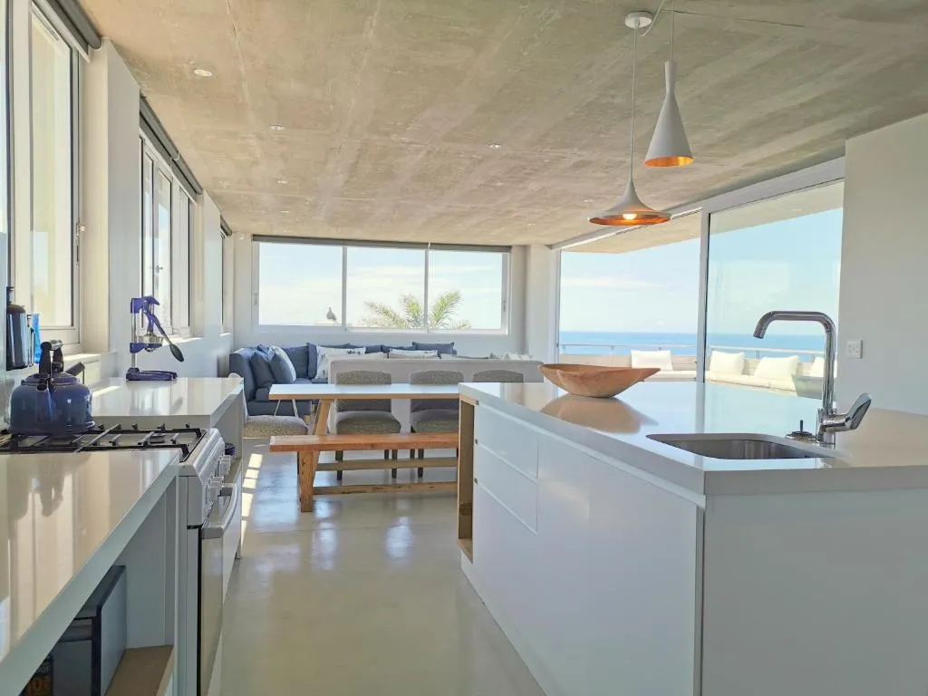 Open-plan kitchen island with a gas hob, dining table and lounge, all facing the ocean