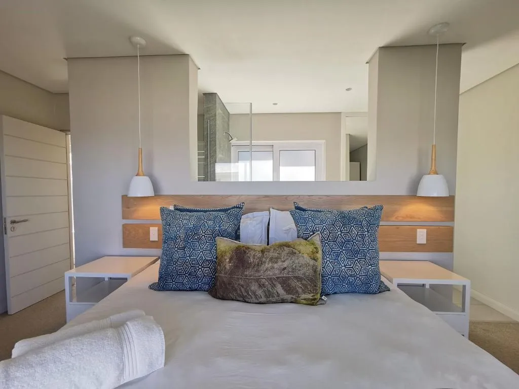 Bedroom with a built-in wood-panelled headboard, pendant lights and an en-suite visible beyond