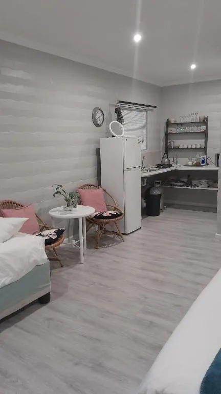 Compact kitchenette with open shelving and a fridge beside a small seating nook with wicker chairs
