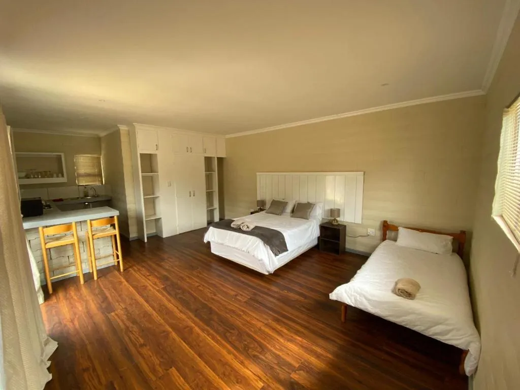 Open-plan studio with a double and single bed beside a breakfast-bar kitchenette on dark wood floors