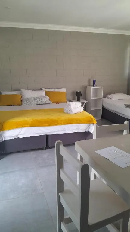 Studio bedroom with two single beds dressed in yellow throws against a bagged-brick wall