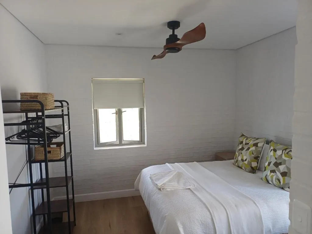 Bedroom with an open clothes rack, patterned scatter cushions and a single window
