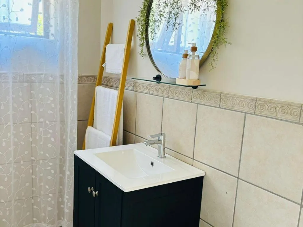 Bathroom vanity with a round mirror, ladder towel rack and tiled splashback