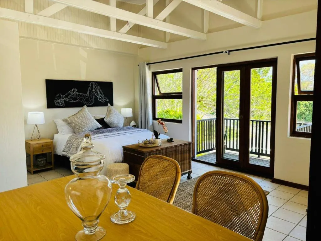 Open-plan bedroom and dining area with a vaulted beam ceiling and French doors onto a treetop balcony