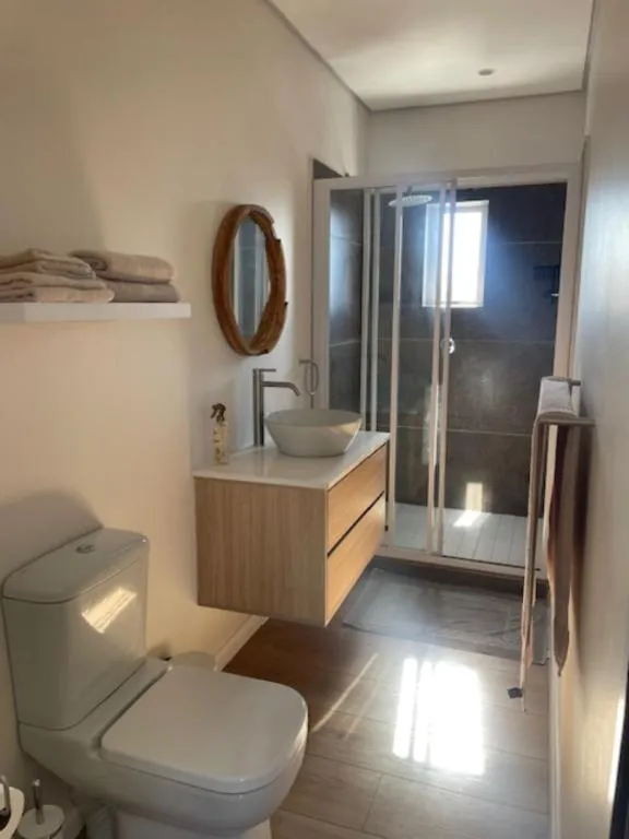 Bathroom with a round vanity mirror, floating wood cabinet and a glass-enclosed shower