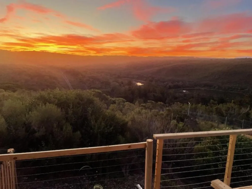 Sunset over a forested valley seen from a deck with a cable-wire balustrade